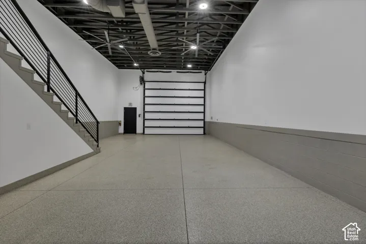 Polished concrete flooring, exposed ceiling structure, recessed lighting, and a roll-up garage door
