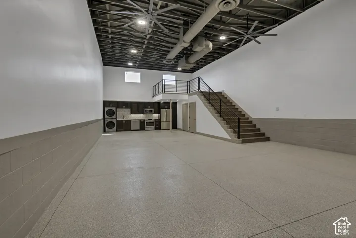 Spacious interior with exposed ceiling ductwork, a built-in kitchen area, and a staircase with metal railings leading to an upper level