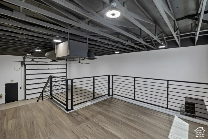 Open loft area featuring wood-finish flooring, industrial-style exposed ceiling beams, and contemporary metal railings