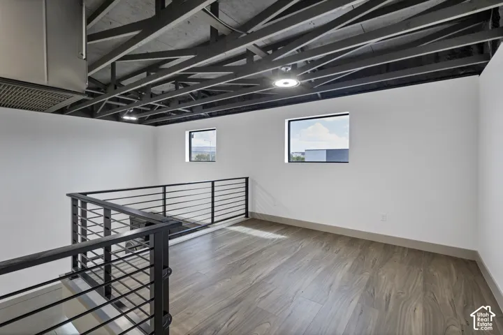 Exposed ceiling joists with recessed lighting, wood-finish flooring, and black metal horizontal bar railing