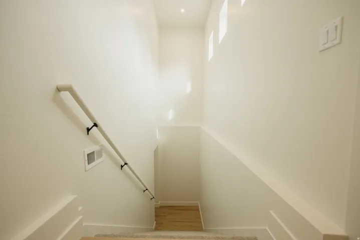 Staircase with light-toned walls, recessed lighting, and wall-mounted handrail
