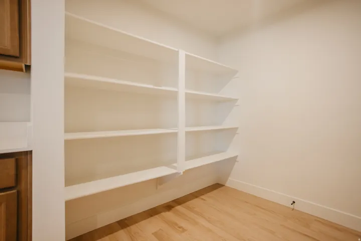 Built-in shelving unit with multiple white shelves, light wood-finish flooring, and white walls