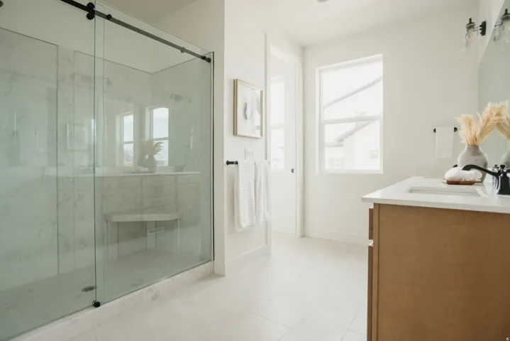 Glass-enclosed shower with a built-in bench, wood-finish vanity with countertop, and tile flooring