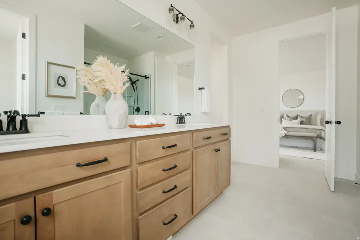 Dual vanity with light wood-finish cabinetry, matte black hardware, and an expansive mirror