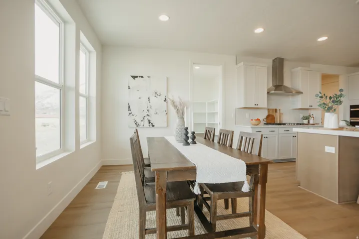 Open-concept kitchen and dining area featuring light wood-finish flooring, white cabinetry, a stainless steel range hood, and recessed lighting