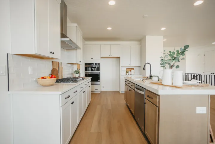 Expansive kitchen with light wood-finish flooring, white cabinetry, integrated stainless steel appliances, a center island with sink, and recessed lighting