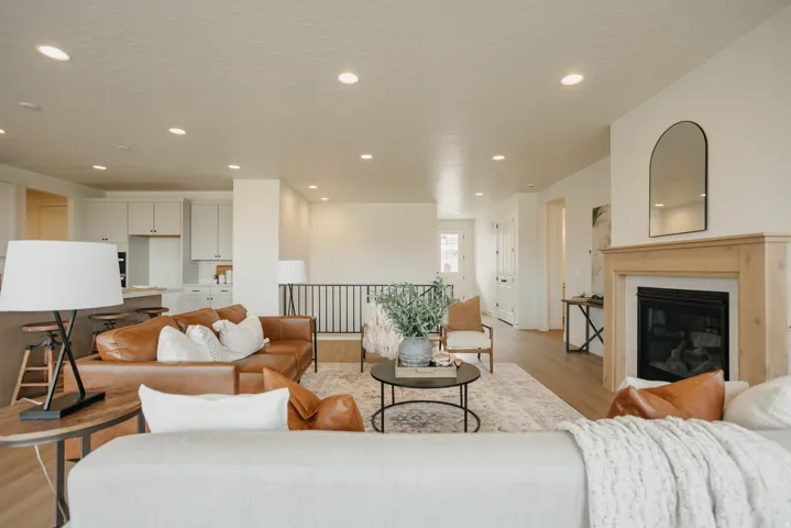 Open-concept living space featuring recessed ceiling lighting, a gas fireplace with wood-finish surround, arched mirror accent, and a mezzanine-level railing