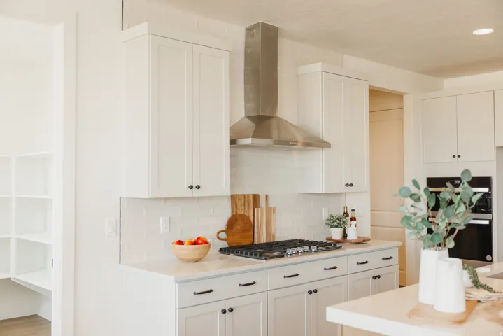 White shaker-style cabinetry with black hardware, stainless steel range hood, built-in gas cooktop, double wall ovens, and a walk-in pantry with built-in shelving