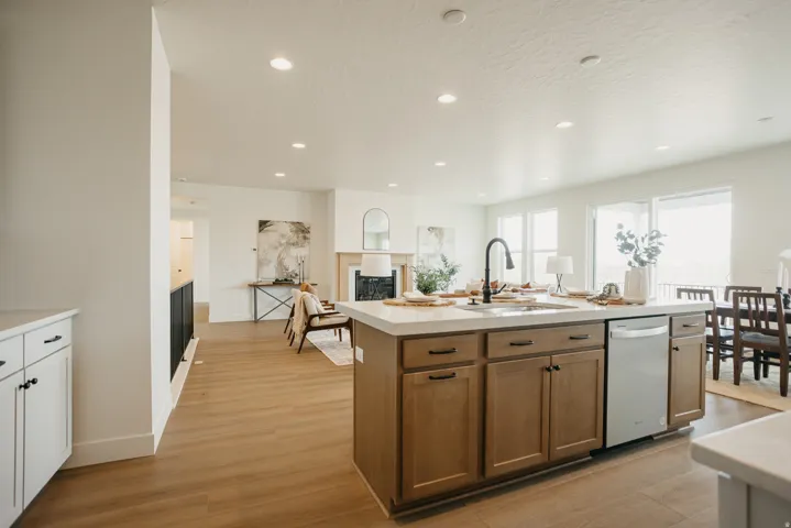 Kitchen island with light wood-finish cabinetry, integrated sink with matte black faucet, and a stainless steel dishwasher