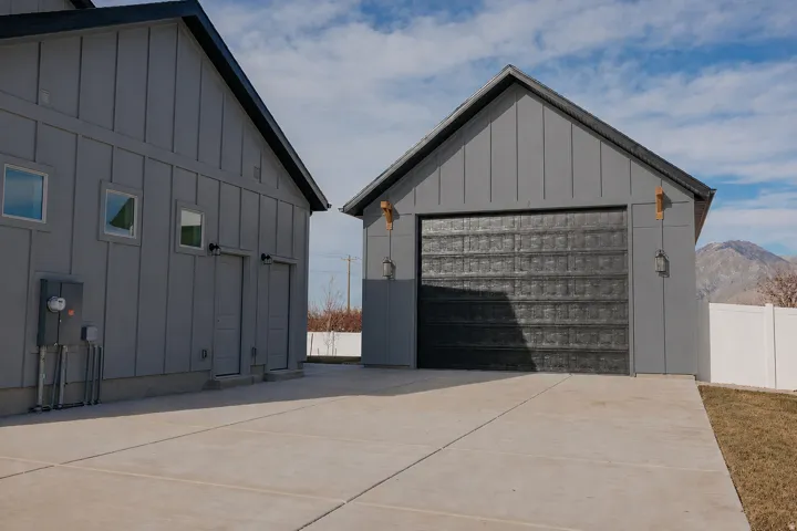 Board and batten siding, dark trim, concrete driveway, and textured garage door