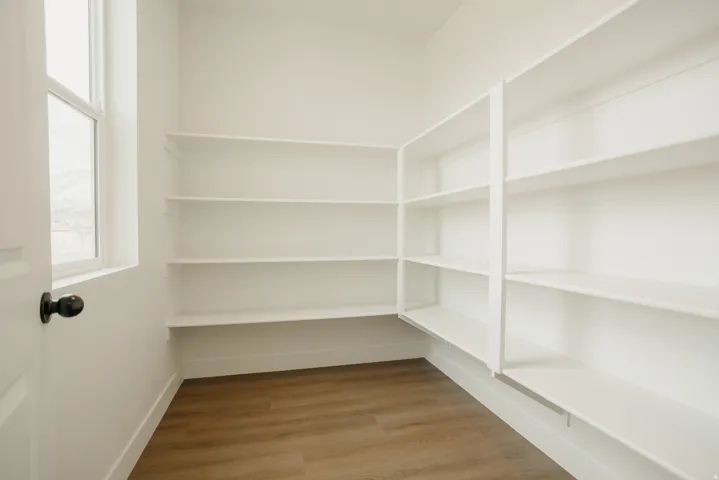 Walk-in pantry featuring extensive white shelving, wood-finish flooring, and a single window