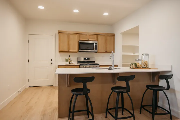 Kitchen featuring light wood cabinetry, stainless steel appliances, a white countertop island with an integrated sink, recessed lighting, and wood-finish flooring