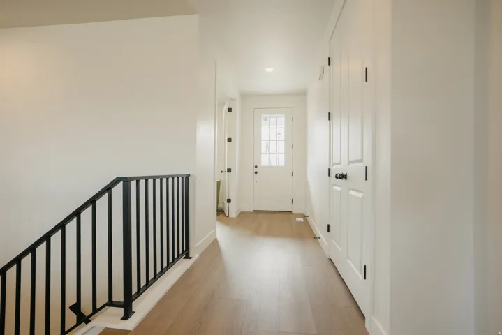 Wood-finish flooring throughout, white paneled doors with matte black hardware, recessed lighting, and a black metal stair railing