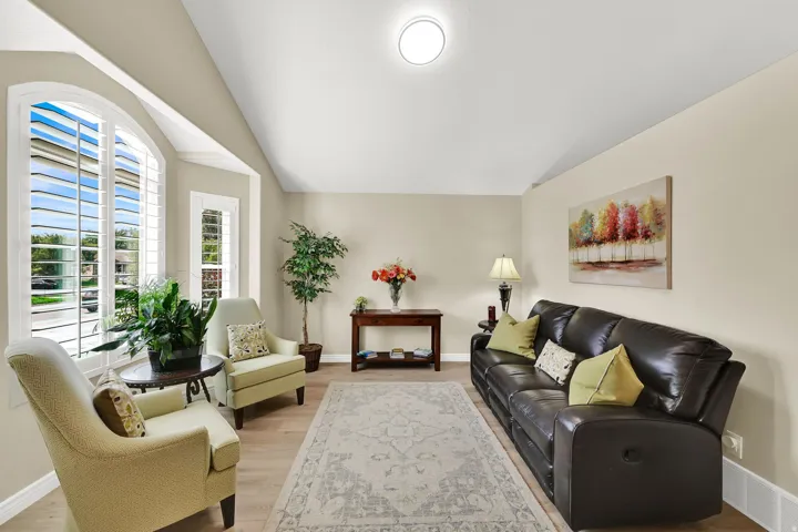 Vaulted ceiling, light-toned walls, arched windows with plantation shutters, wood-finish flooring, and a decorative ceiling light fixture