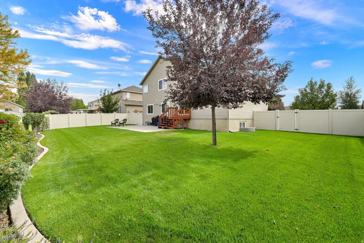Expansive green lawn, concrete patio, wood deck with stairs, mature tree, and privacy fencing