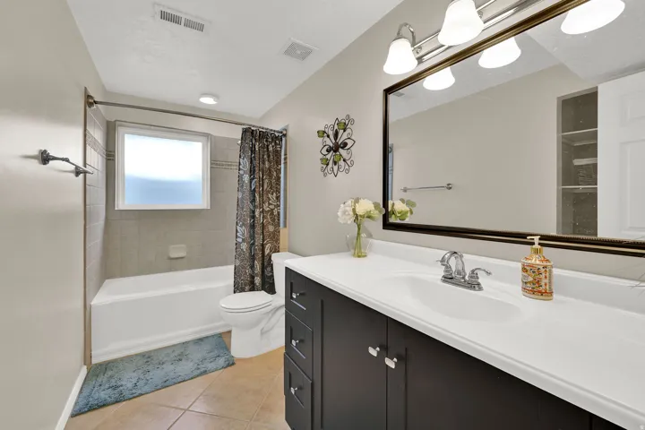 Bathroom featuring a dark wood finish vanity with integrated sink, a large framed mirror, and a combination tub and shower with tiled surround