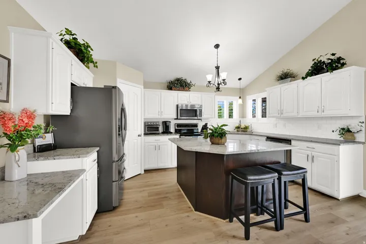 Kitchen featuring white cabinetry, light-toned countertops, a central island with bar seating, wood-finish flooring, and a vaulted ceiling