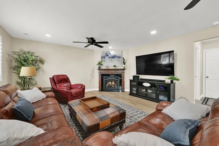 Recessed lighting illuminates the room, featuring wood-finish flooring, a corner fireplace with a dark wood mantel, and ceiling fans