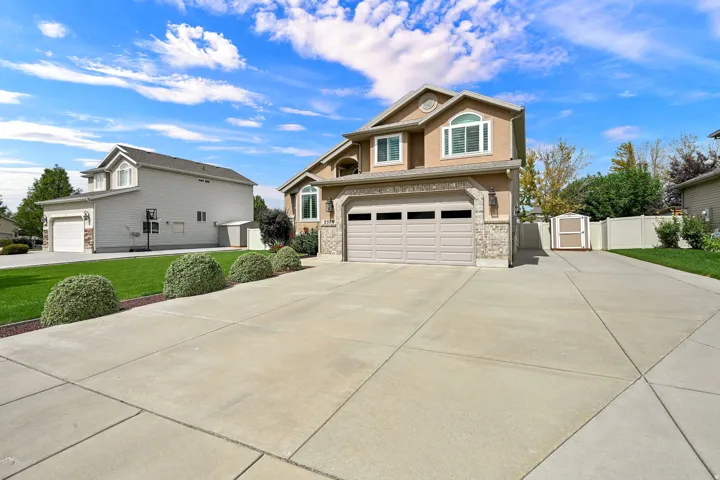Stucco exterior with stone accents, arched window, two-car garage, concrete driveway, and well-maintained landscaping
