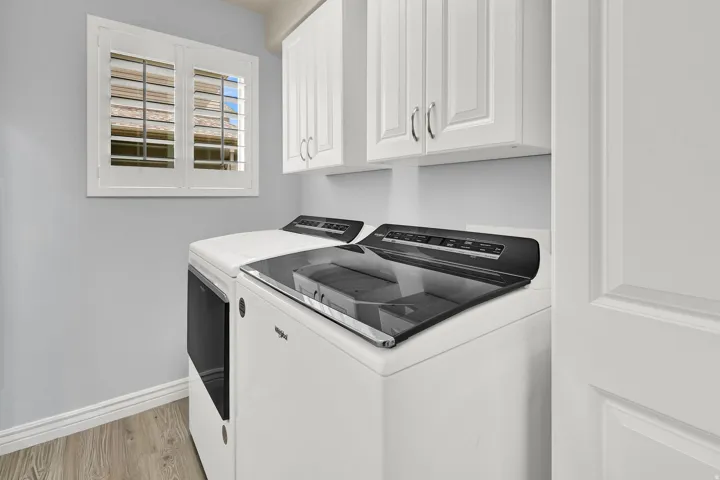 White shaker-style cabinetry, wood-finish flooring, white plantation shutters, and a paneled interior door