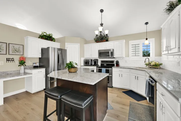 Kitchen featuring white cabinetry, light-toned wood-finish flooring, a central island with a contrasting dark wood base, stainless steel appliances, and light-colored countertops with a subway tile backsplash