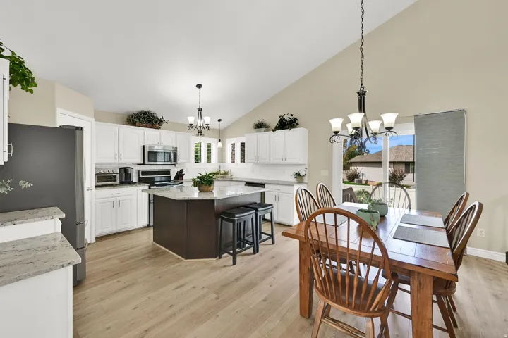 Vaulted ceilings, wood-finish flooring, white cabinetry, dark-finish kitchen island with seating, and a sliding glass door