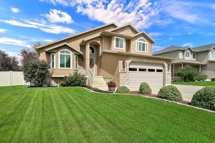 Stucco exterior with stone accents, arched entry, bay window, two-car garage, and mature landscaping
