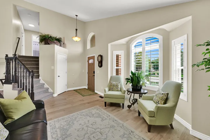 Soaring ceilings with a decorative pendant light, wood-finish flooring, and a bay window featuring white plantation shutters