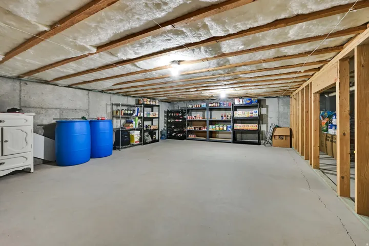 Unfinished basement with exposed wood joists and insulation, concrete walls, concrete flooring, and partial wood framing
