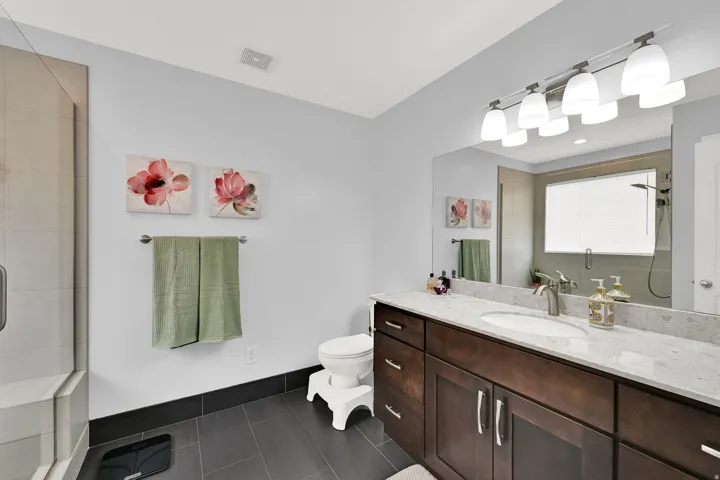 Spacious bathroom featuring a glass-enclosed shower, dark wood-finish vanity with dual sinks, substantial mirror, and a five-light fixture