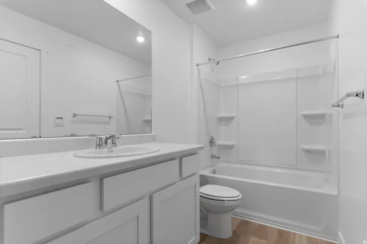 White vanity with an integrated sink, polished chrome faucet, full-width mirror, and a white tub/shower combination with integrated shelving