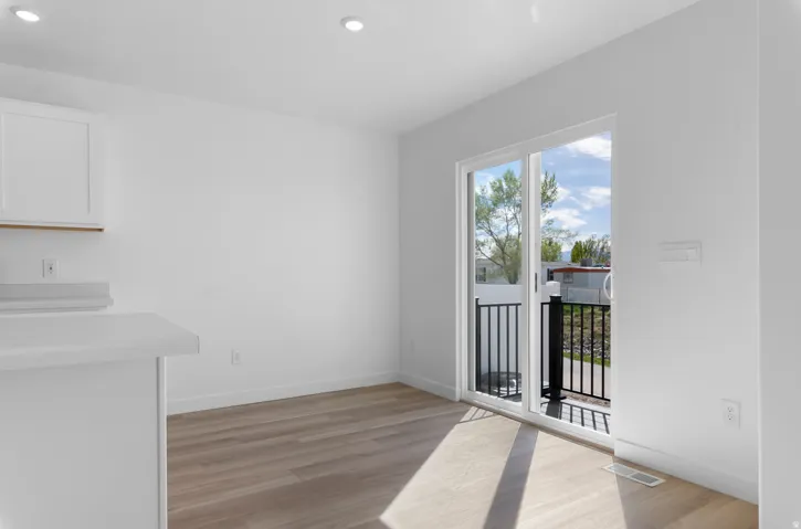 Recessed lighting, wood-finish flooring, white walls, white cabinetry, and sliding glass door with black metal railing