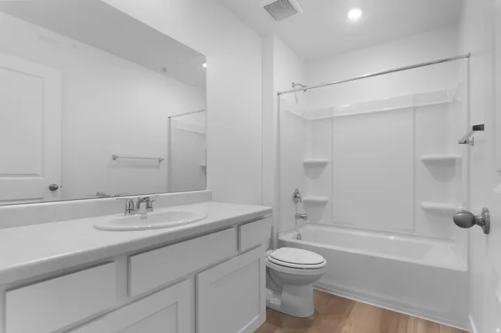 White vanity with an integrated sink and chrome faucet, large wall-mounted mirror, and wood-finish flooring