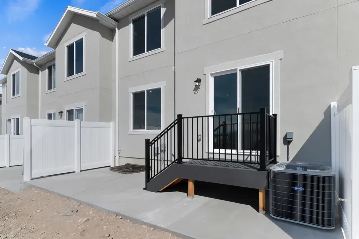 Rear exterior featuring a sliding glass door, private deck with black railings, and concrete patio