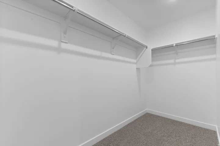 Walk-in closet featuring white walls, gray carpeting, and integrated shelving with chrome hanging rods