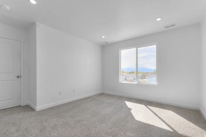 Recessed lighting, light gray carpeting, crisp white walls, and a large window