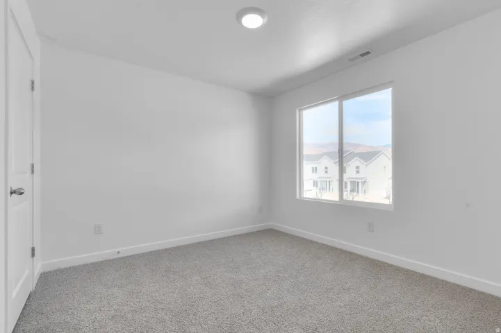 White walls, gray carpet, single window, white door, overhead lighting