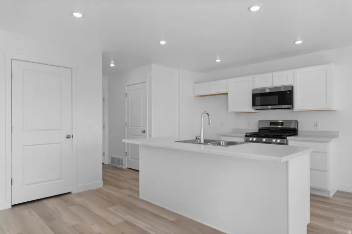 Kitchen featuring white cabinetry, stainless steel appliances, a center island, and wood-finish flooring
