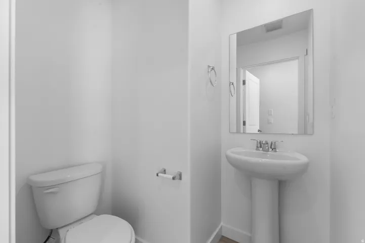 Pedestal sink with chrome fixtures, wall-mounted mirror, and white toilet