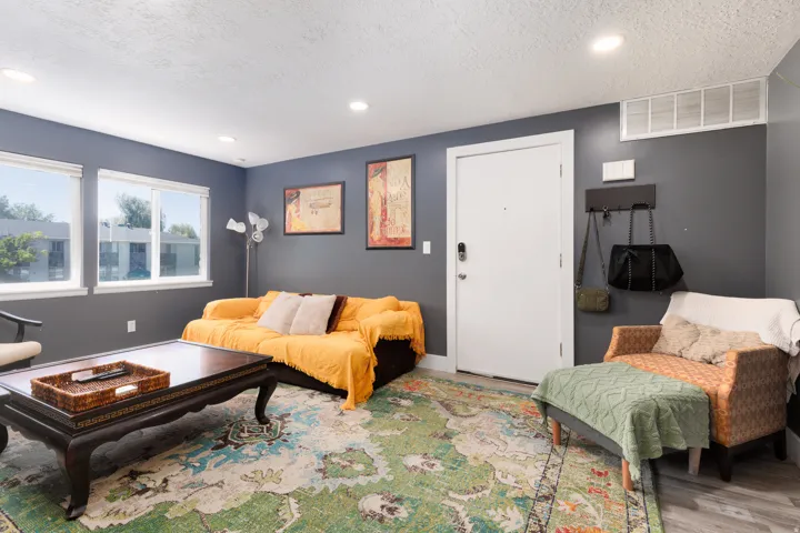 Recessed ceiling lighting, multiple large windows, wood-finish flooring, and a white entry door