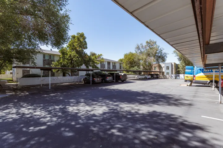 Paved parking area with covered parking structures and mature trees