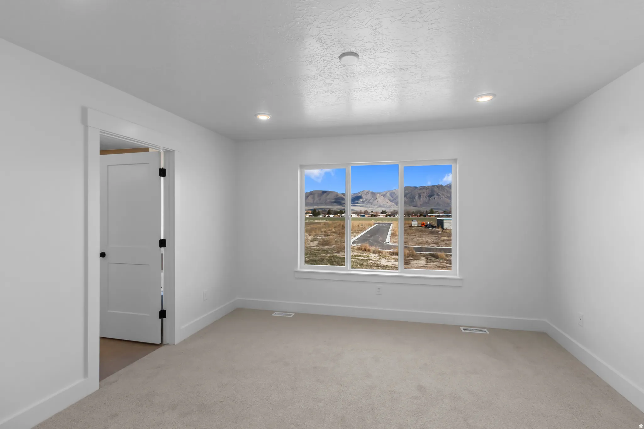 Recessed lighting, light-toned carpeting, white interior walls, white trim, and a white interior door with black hardware