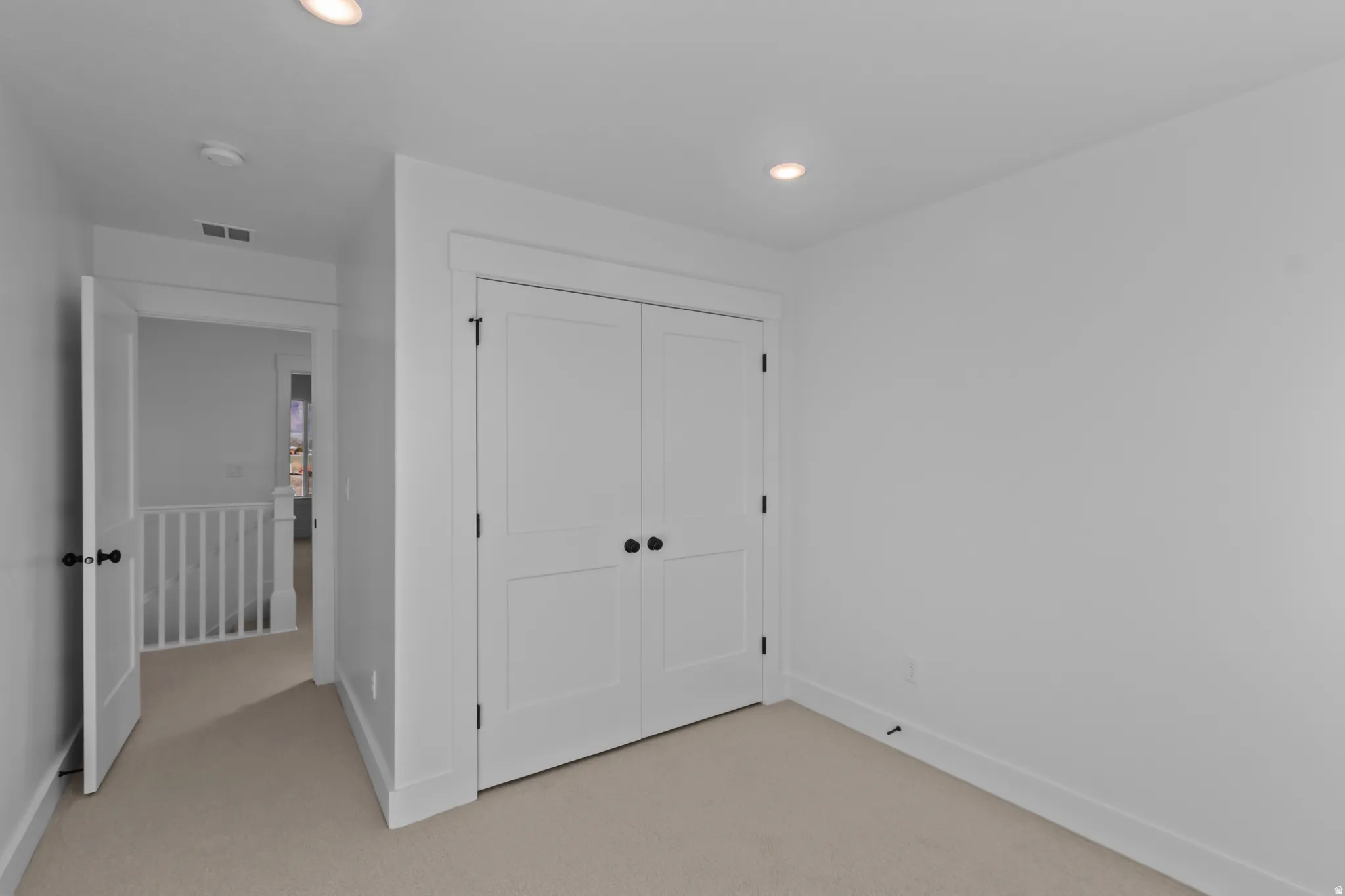 Neutral tone wall paint, recessed ceiling lighting, two-panel closet doors with dark hardware, and plush carpet flooring