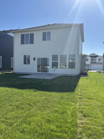 Two-story exterior with light-colored siding, a concrete patio, and a grass lawn