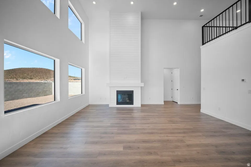 Spacious living area featuring high ceilings, wood-finish flooring, a contemporary fireplace with a shiplap surround, and multiple large windows