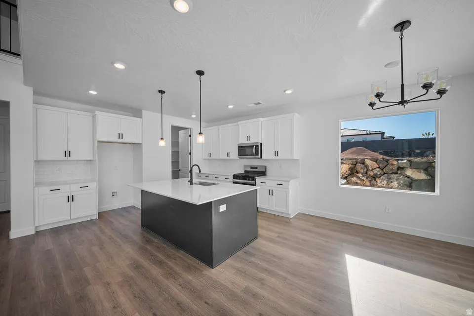 Open-concept kitchen with wood-finish flooring, white cabinetry, and a dark-toned island with a white countertop