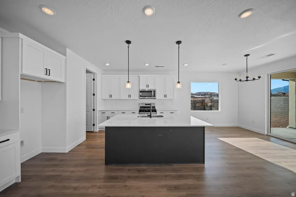 White cabinetry with dark hardware, a dark kitchen island, stainless steel appliances, wood-finish flooring, and a sliding glass door