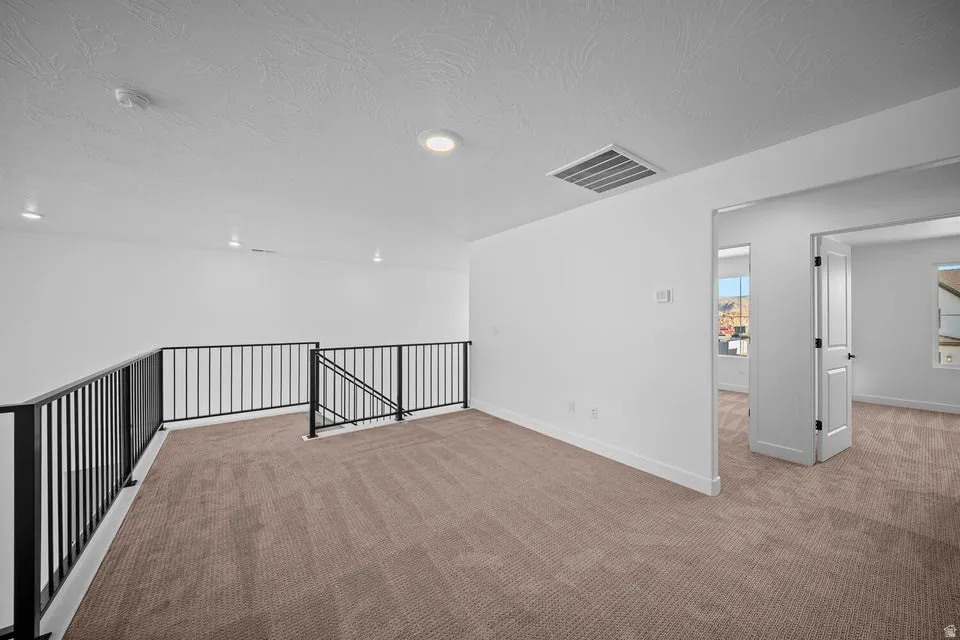 Carpeted loft area featuring black metal railing, recessed lighting, and white interior walls