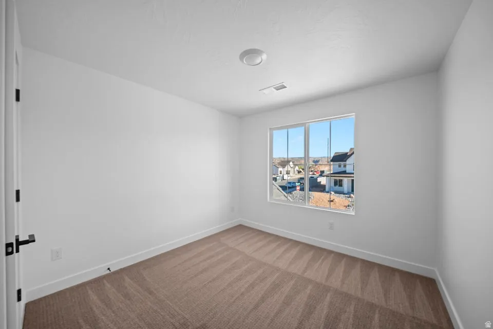 Neutral white wall finishes, brown patterned carpeting, white window frames, modern black door hardware, and a ceiling-mounted light fixture