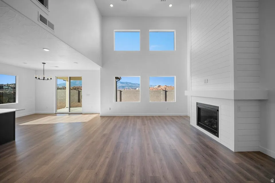 Spacious living area featuring high vaulted ceilings, large windows, wood-finish flooring, a contemporary fireplace with a shiplap surround, and a sliding glass door leading to an outdoor area